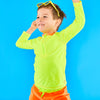 Child posing playfully wearing neon yellow sunglasses and neon yellow rash guard and neon orange swim trunks